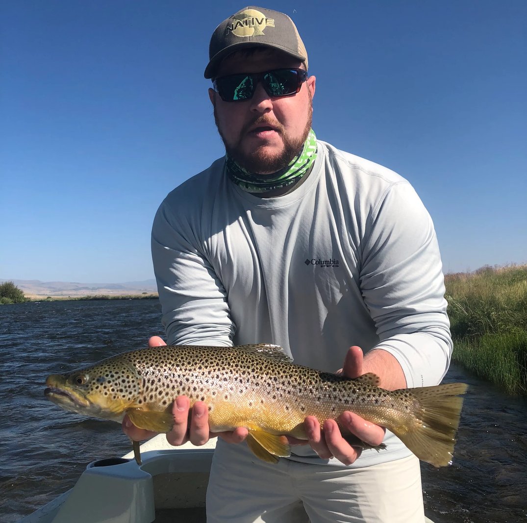 Angler in sunglasses holding a large Brown Trout in a river.