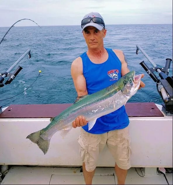 Angler holding a large Steelhead on a boat with fishing rods in the background