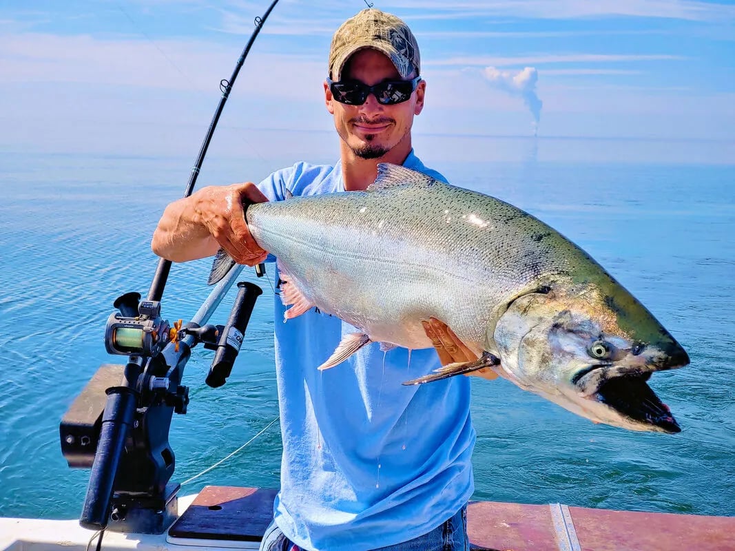 Angler holding a large salmon-like fish on a boat under a clear sky