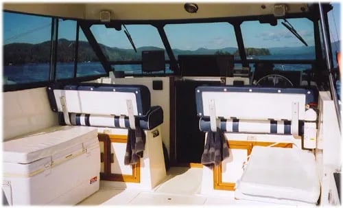 Interior view of a fishing boat cabin with two white and blue striped seats and a cooler