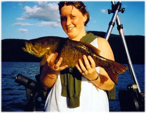 Young boy holding a large Lake Trout on a boat under a bright blue sky