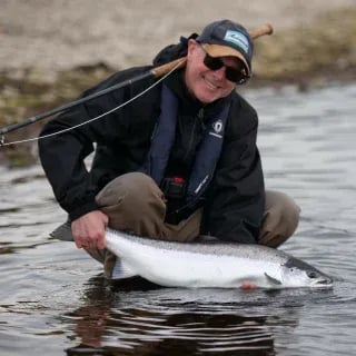 Angler holding a vibrant Atlantic Salmon in shallow river water