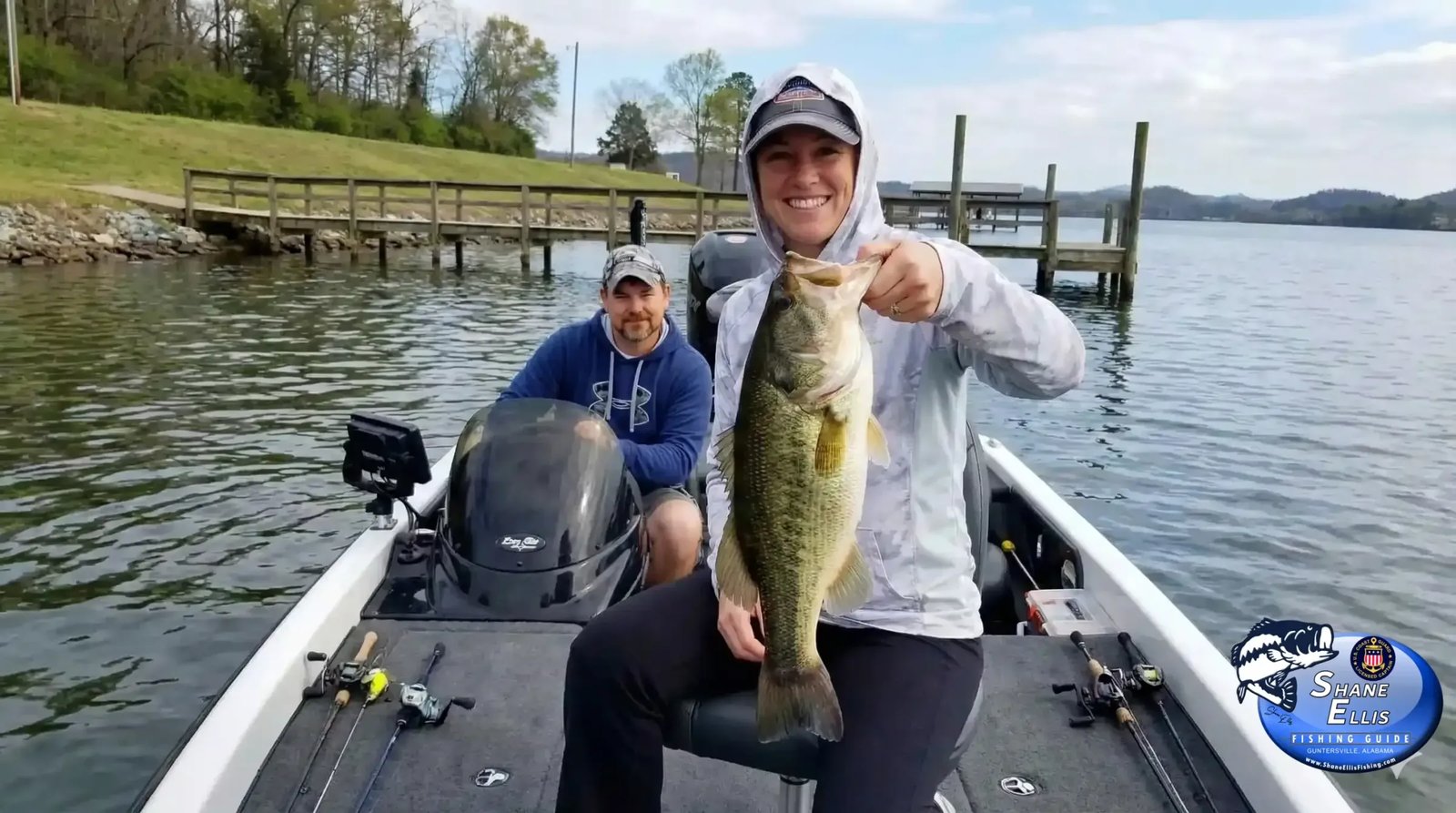 Two anglers in a bass boat, one holding a Largemouth Bass.