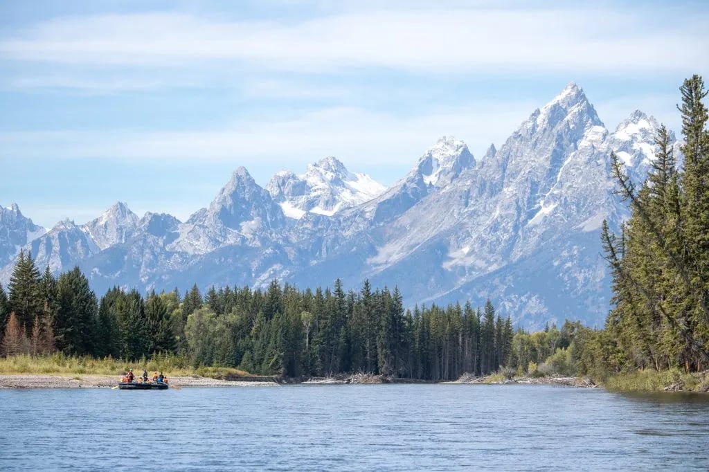 Raft with passengers floating on a wide river with the Grand Teton mountains in the background