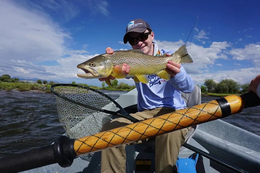 Angler in a drift boat proudly holding a large Brown Trout