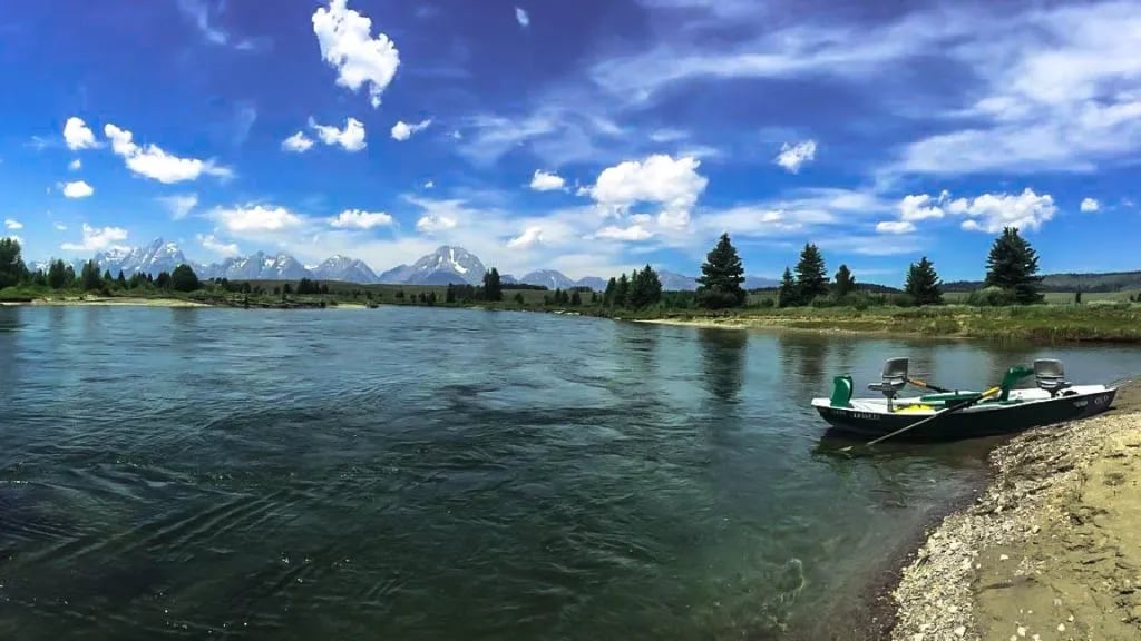 Drift boat pulled onto a sandy bank of the Snake River with the Teton mountains under a blue sky