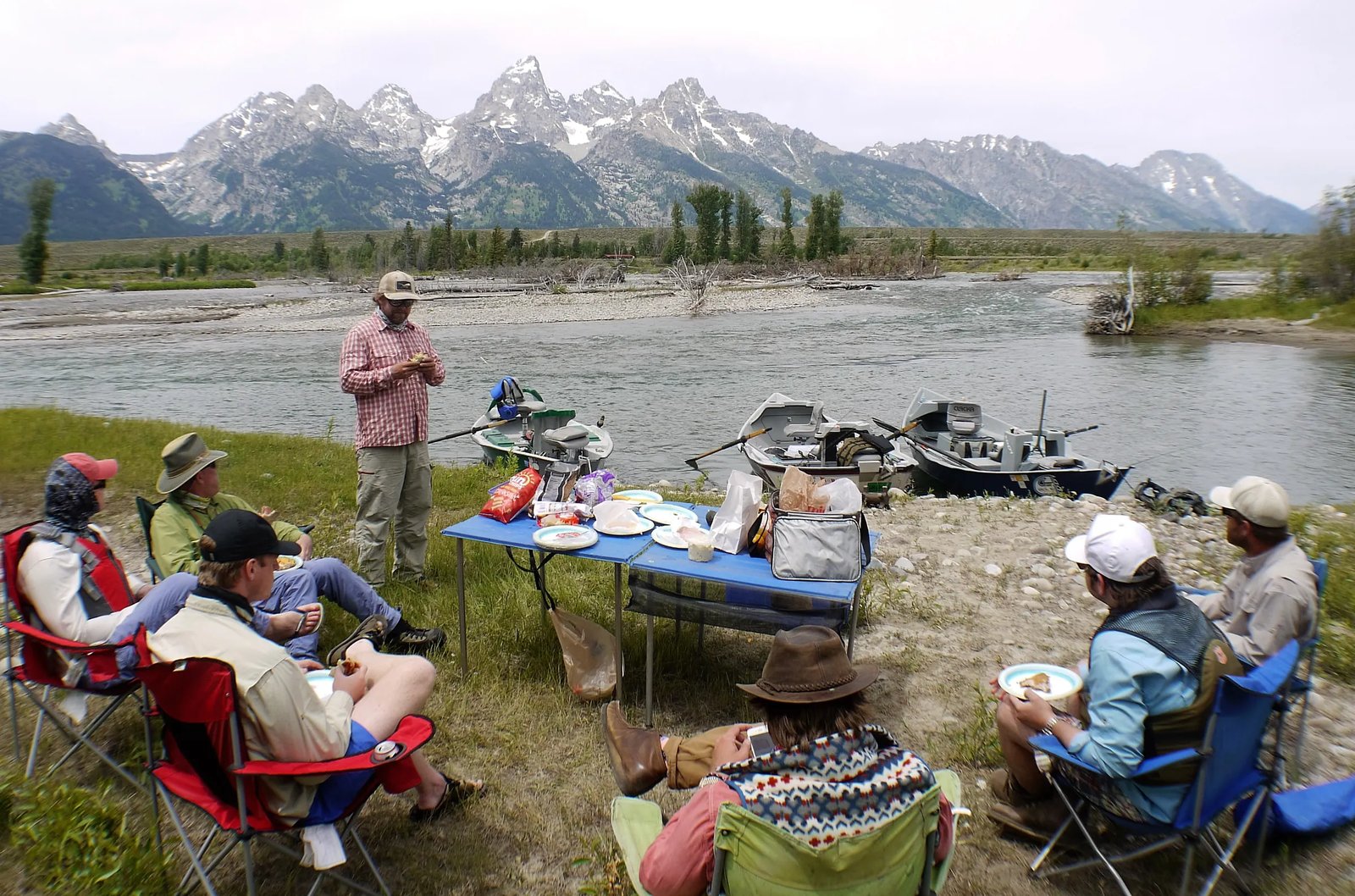 Anglers enjoying a riverside lunch with drift boats and the Teton mountain range in the background