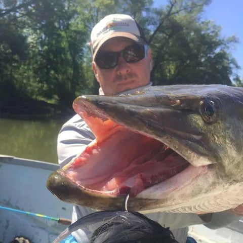 Angler smiling in a river, holding a Steelhead.