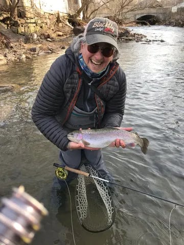 Angler in sunglasses holding a small fish over a rocky stream.