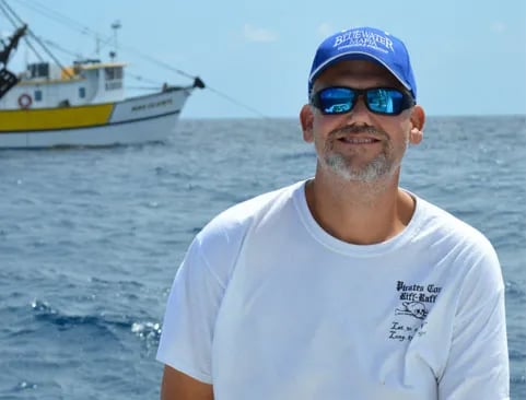 White sportfishing boat with a tower floating on clear blue ocean water.