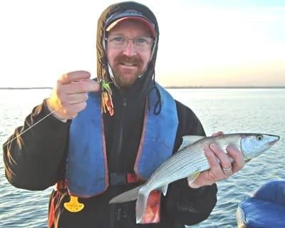 Man in a life vest holding a bonefish and a jig on the water.