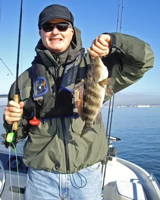 Angler in sunglasses holding a calico bass on a boat.