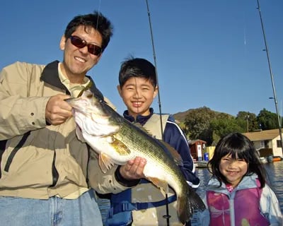 Man and two children smiling while holding a large largemouth bass.