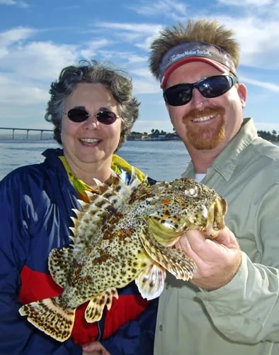 Two anglers holding a spiny sculpin with a bridge in the background.