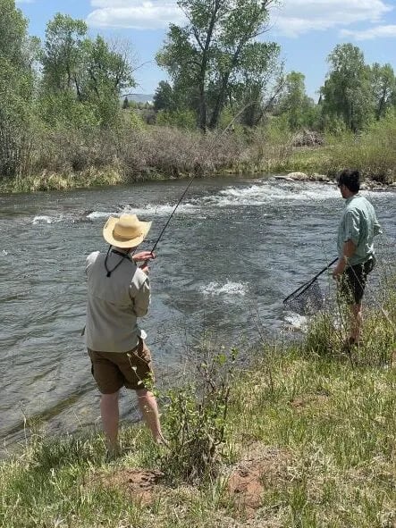 Two anglers wading and fly fishing in a wide, rocky river.