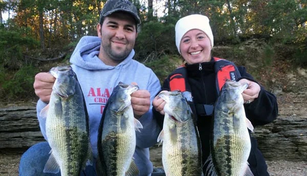Two smiling anglers hold up four freshly caught Largemouth Bass.