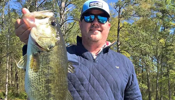 Angler in sunglasses and a blue cap holds a large Largemouth Bass.