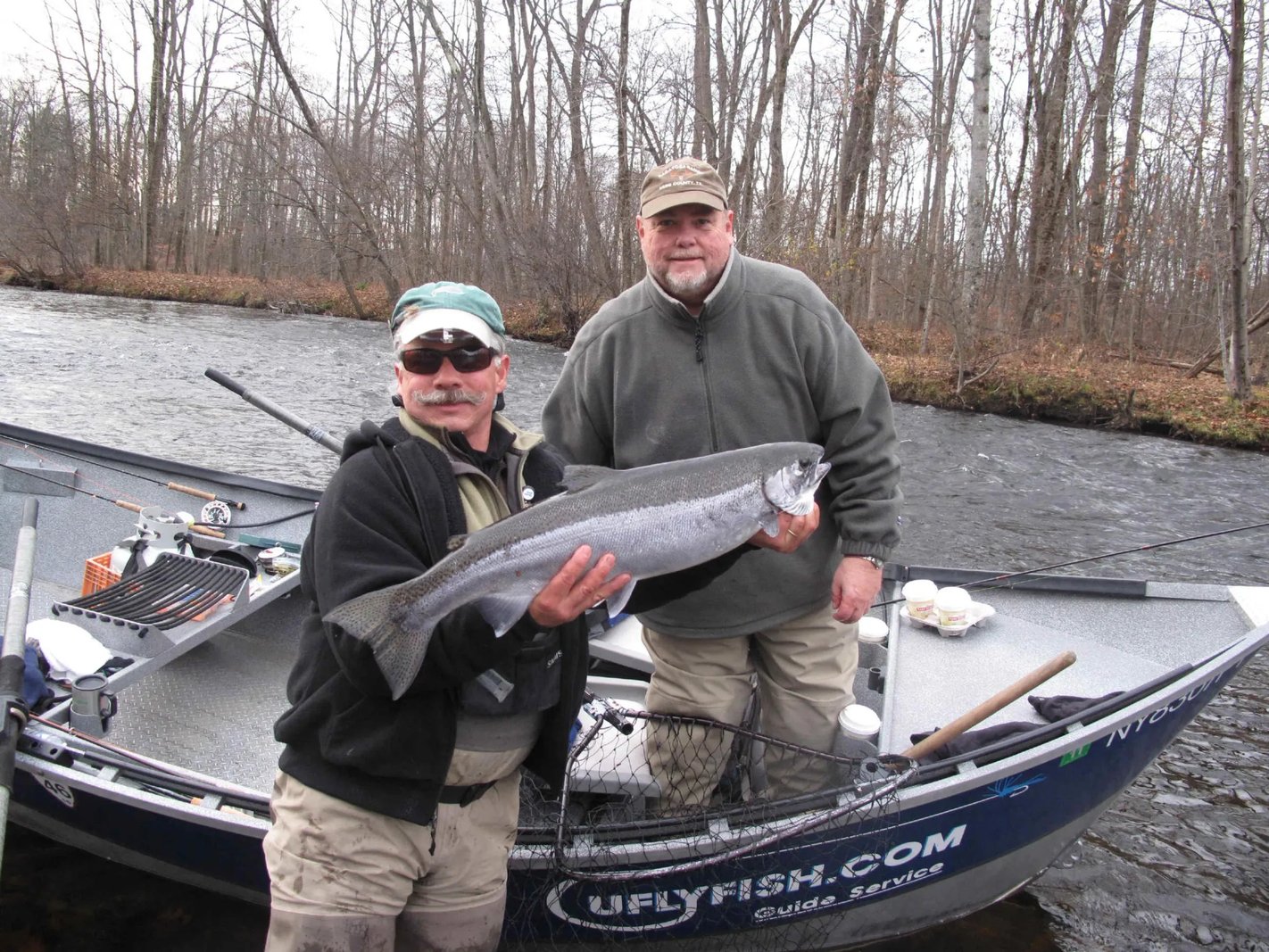 Angler in sunglasses and a cap in a drift boat on a river with forested banks