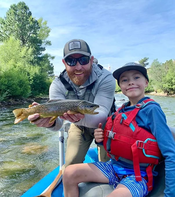 Man holding a Brown Trout with a child in a raft on a sunny river