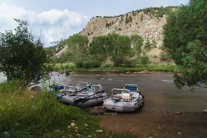 Two rafts pulled up on a river bank with a rocky mountain backdrop