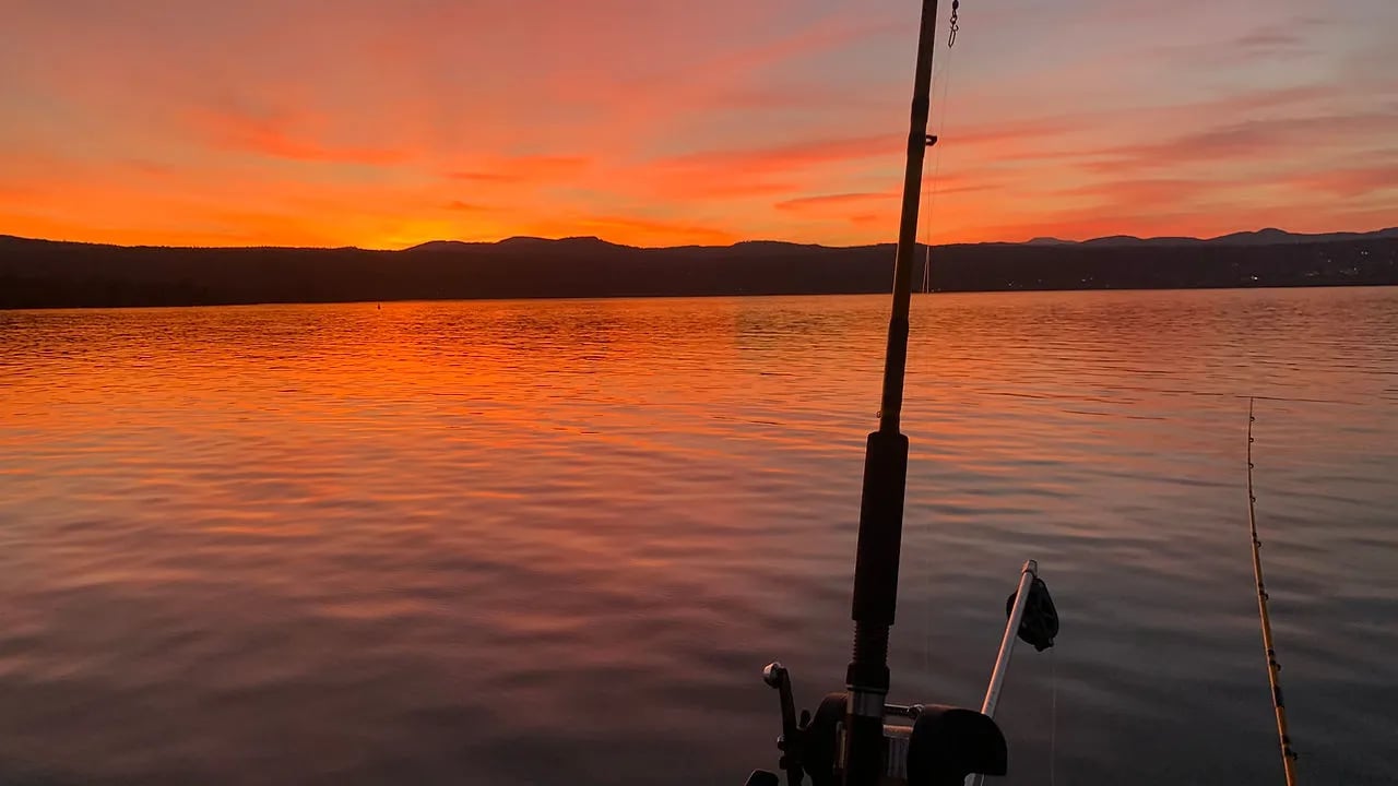 Fishing rod silhouetted against a vibrant orange and purple sunset over calm water