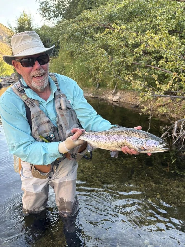 Angler in waders holding a large Brown Trout in a river with mountains in the background
