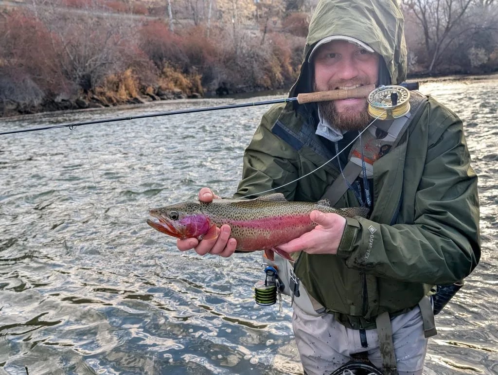 Angler in a hat and sunglasses holding a Rainbow Trout in a shallow river