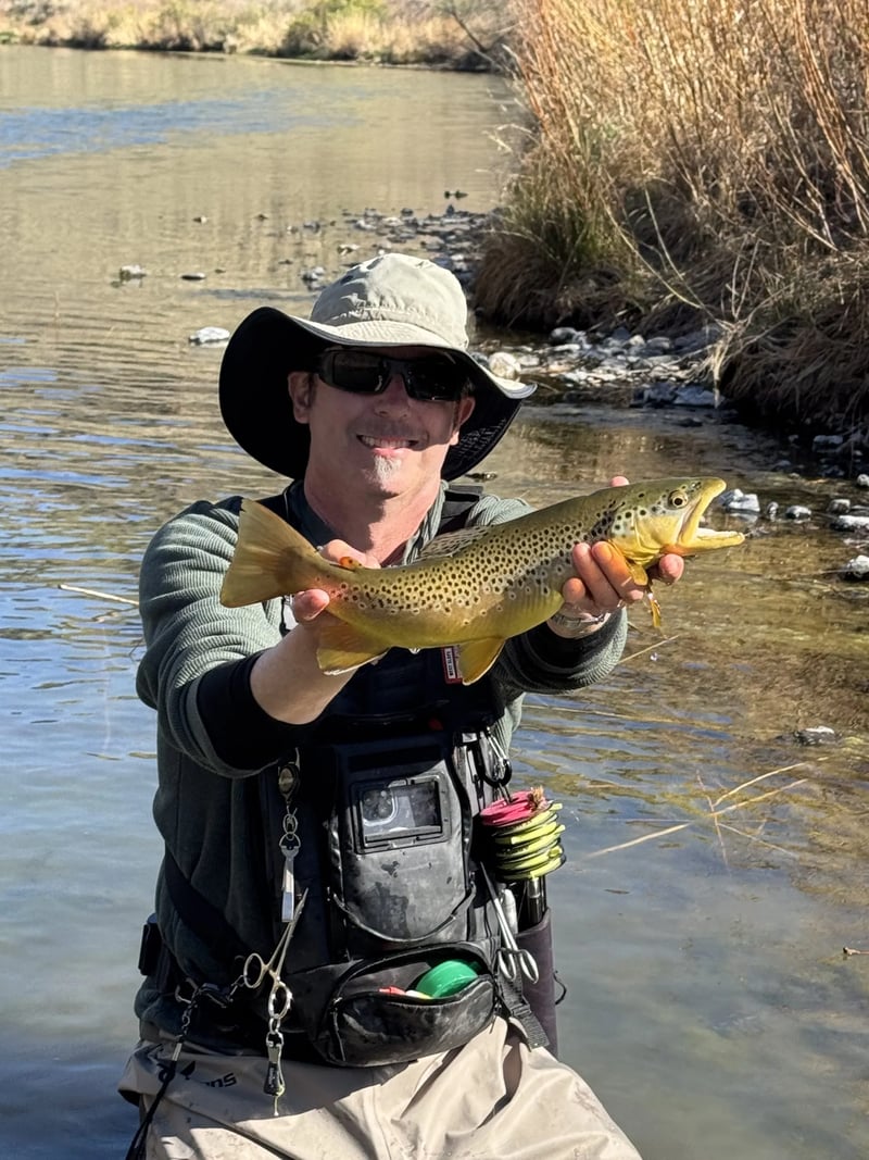 Angler in a hooded jacket holding a Rainbow Trout with a fly rod in their mouth