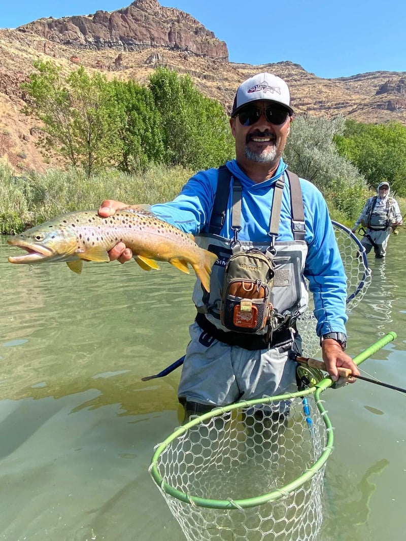 Angler in a wide-brimmed hat holding a spotted Brown Trout in a sunlit river