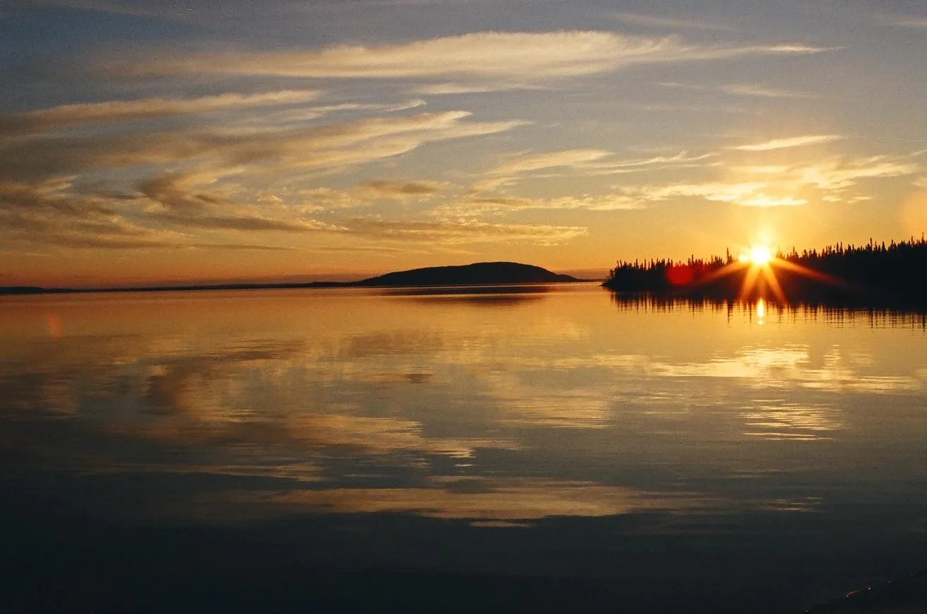 Sunset over a calm lake with a distant treeline and island