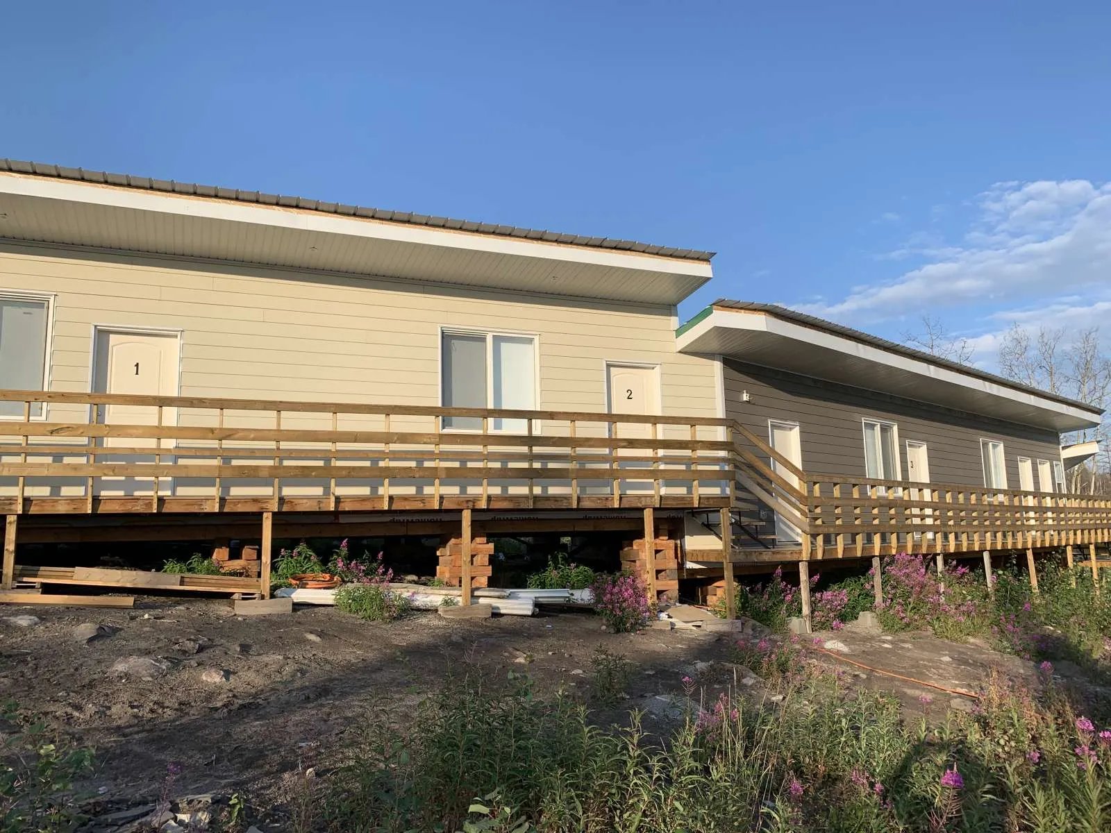 Two long, low cabin buildings with wooden decks and ramps on a grassy slope