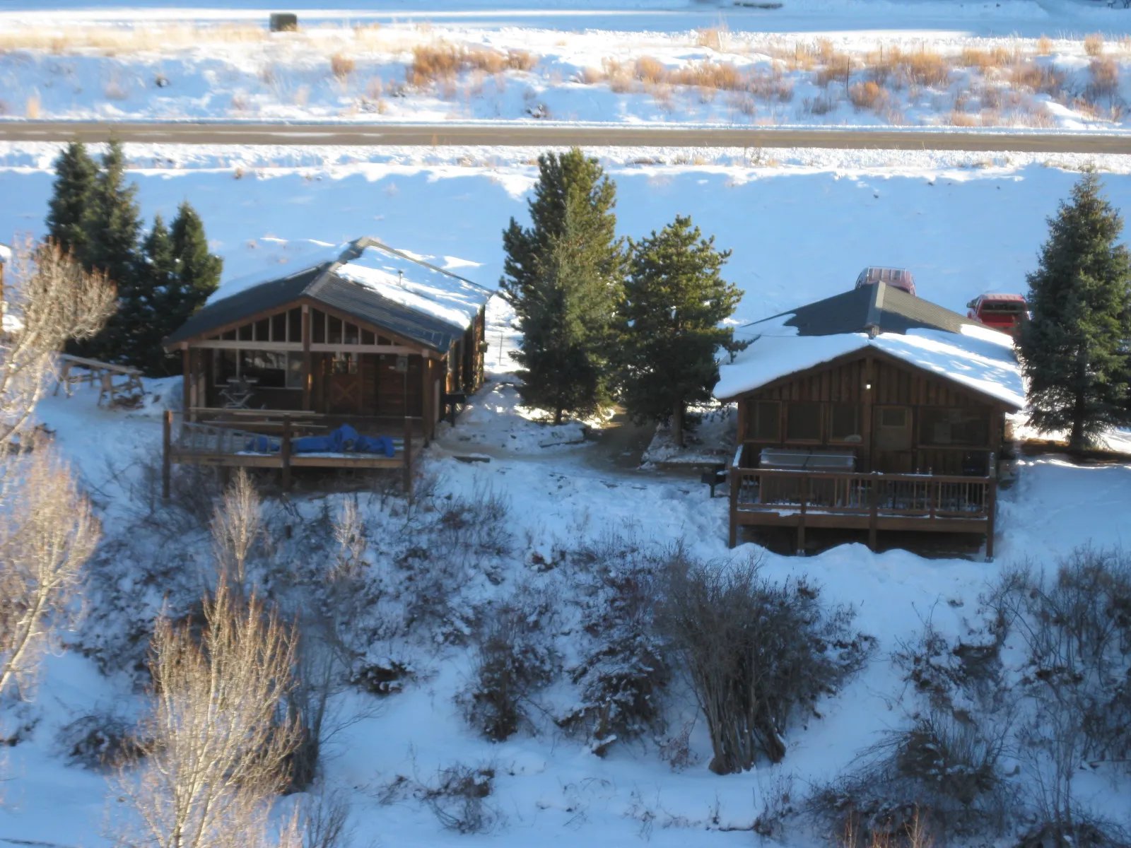 Two cabins with snow-covered roofs and decks overlooking a frozen river