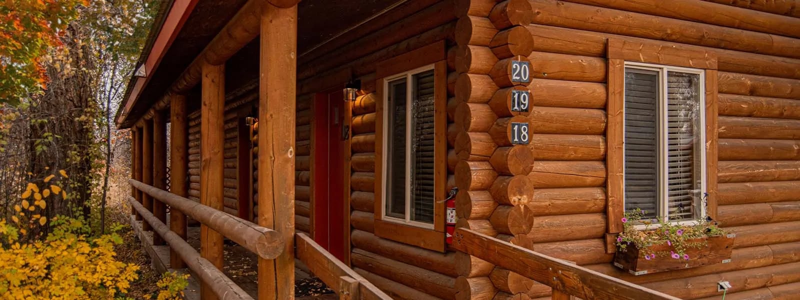 Exterior of a log cabin with a red roof and fall foliage
