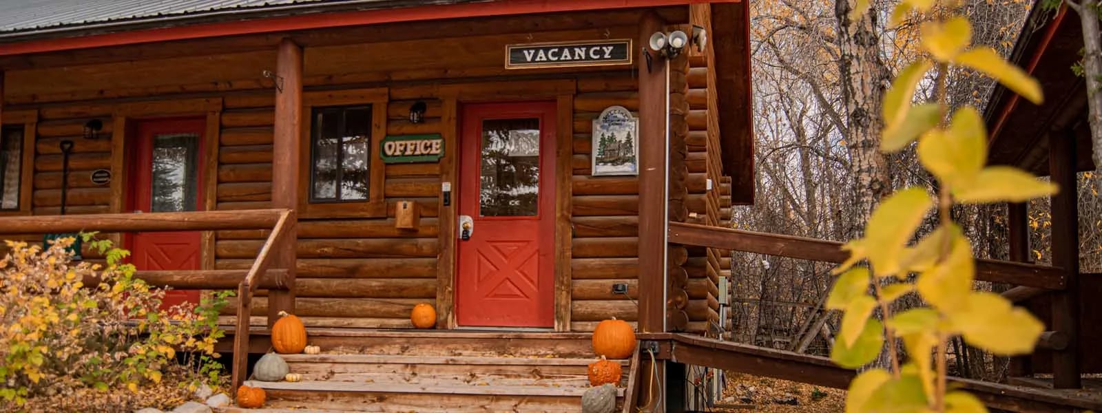 Log cabin entrance with a red door and pumpkins on the porch in autumn