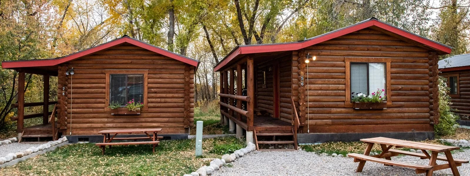 Two rustic log cabins with red roofs and picnic tables outside