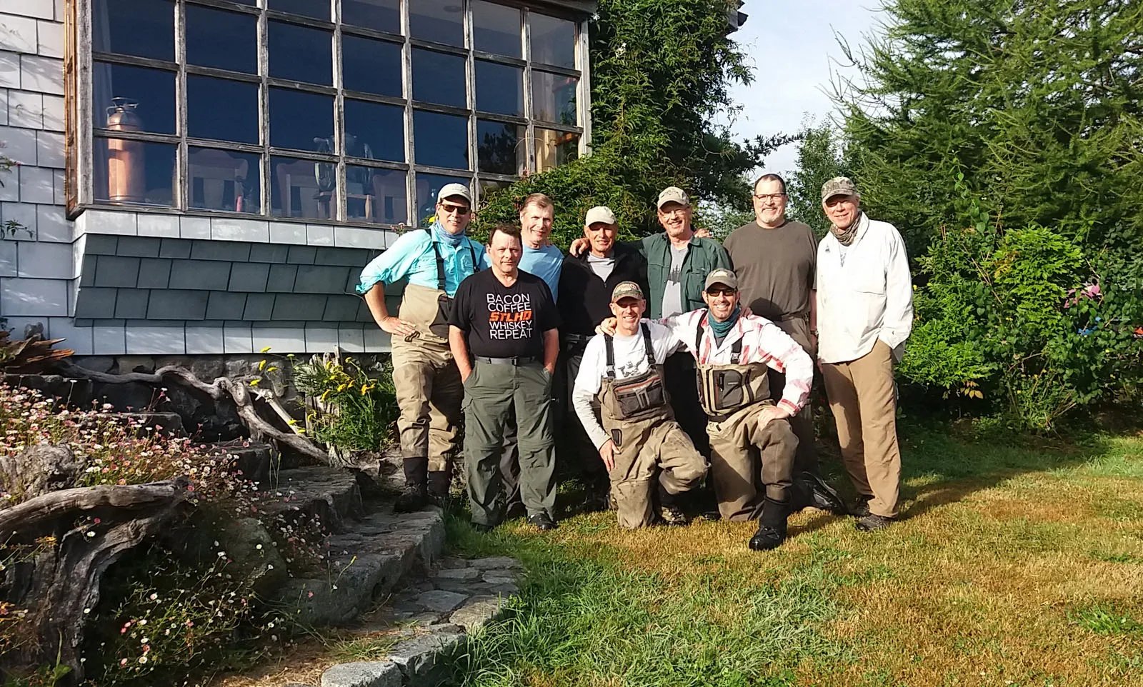 Group of eight fishermen posing in front of the lodge exterior.