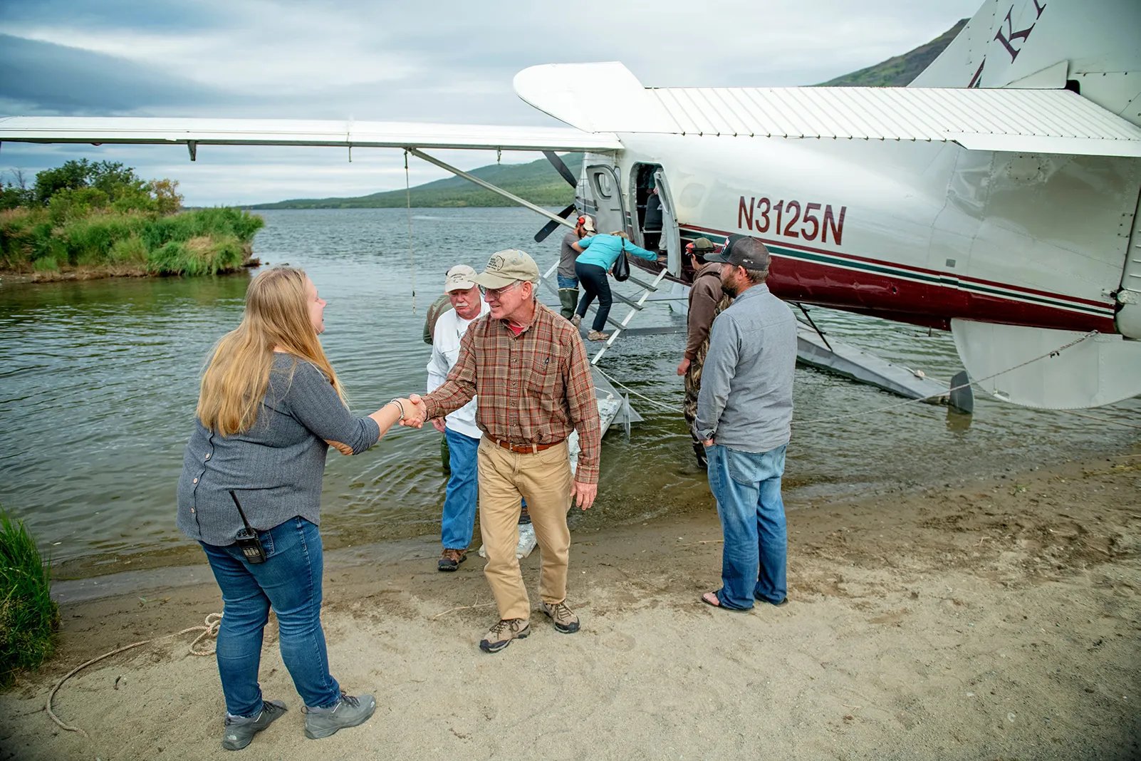 Guests shaking hands with lodge staff after disembarking a floatplane on a sandy beach at Kulik Lodge