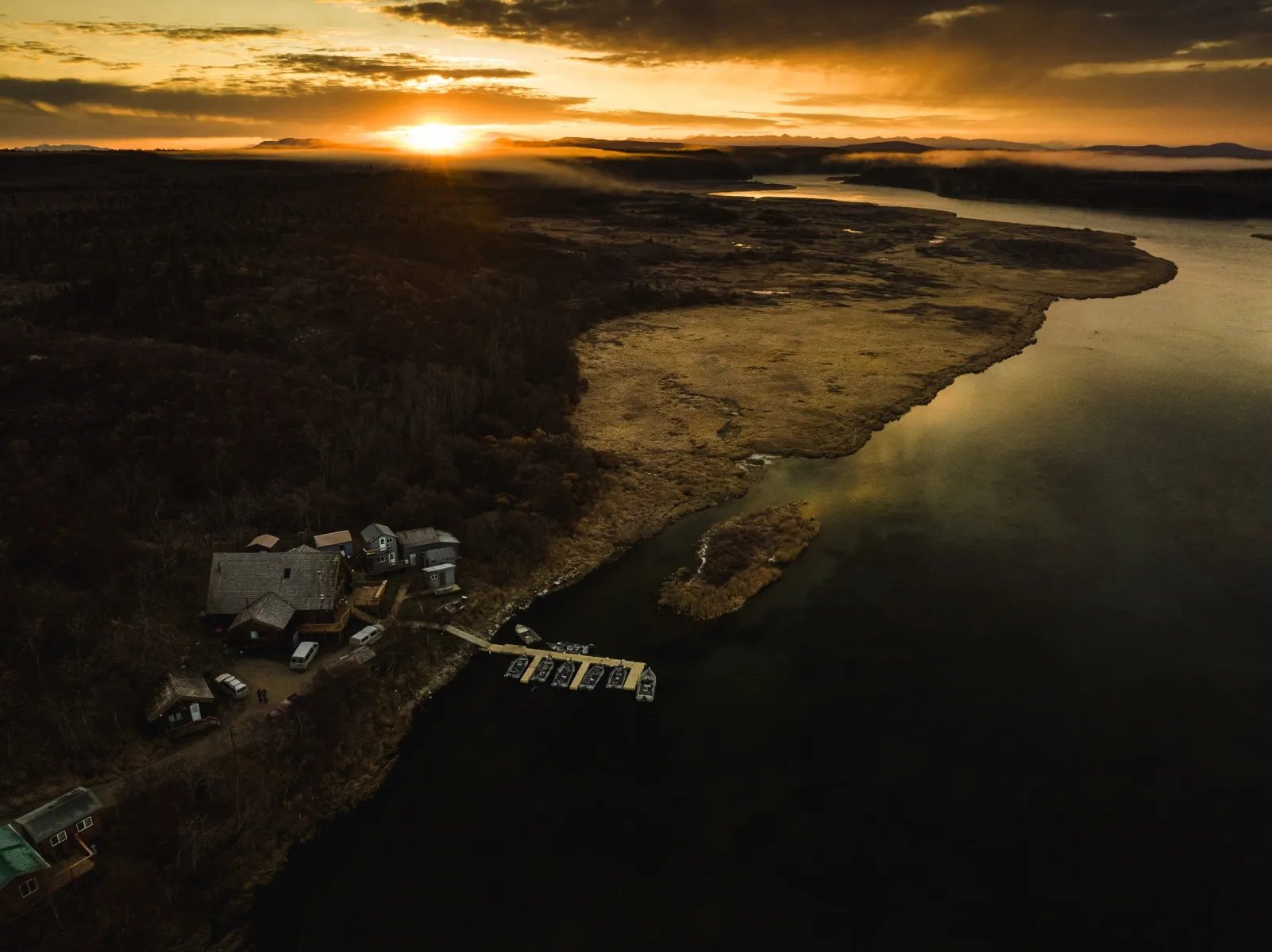 Aerial view of Katmai Trophy Lodge and dock on a river at sunset, surrounded by autumn trees.