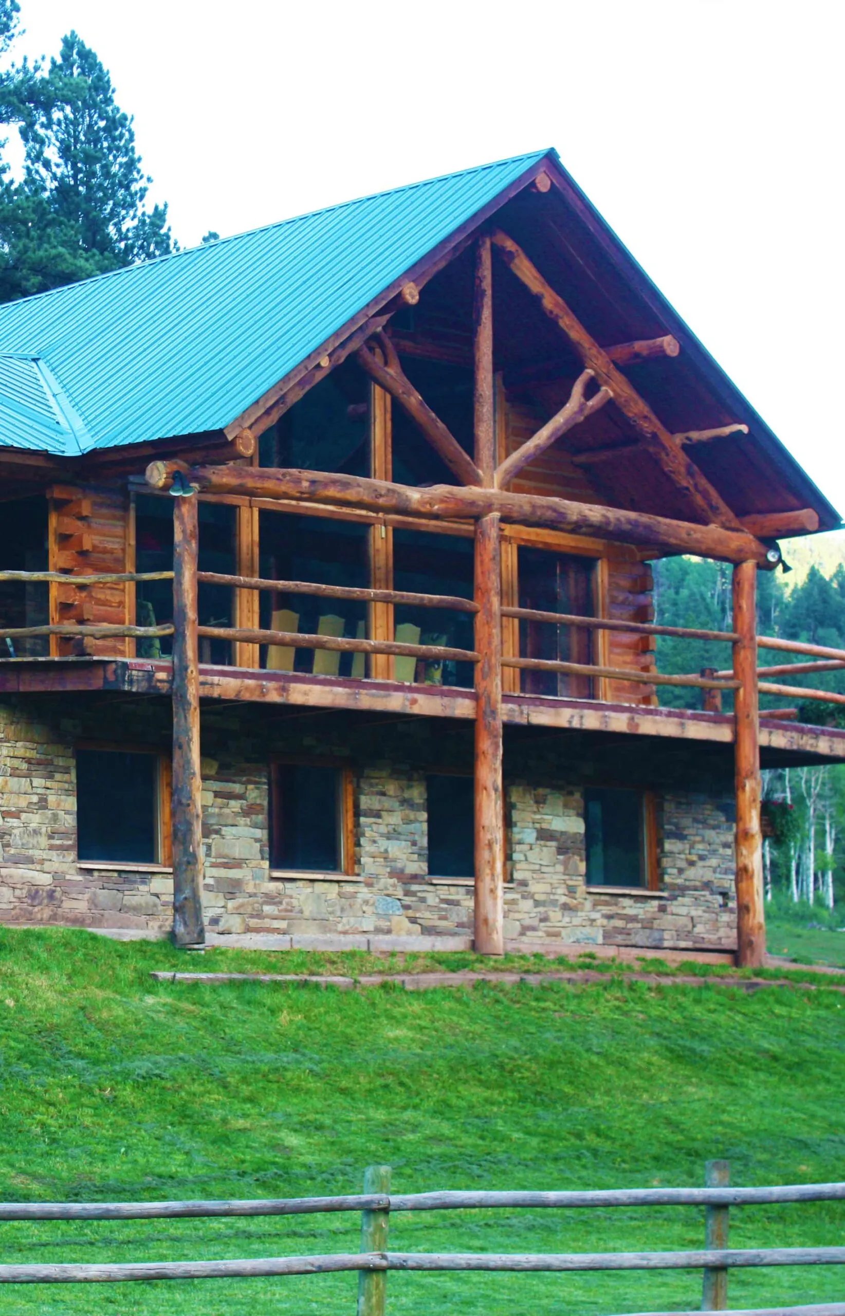 Rustic log cabin lodge with a bright green roof and stone base, surrounded by green grass