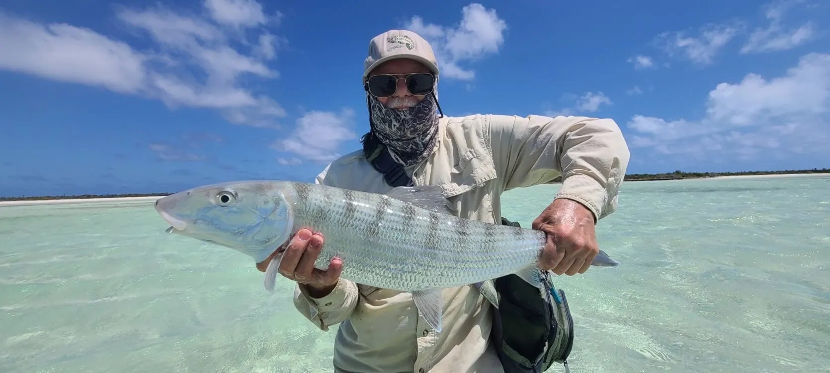 Angler in a hat and buff holding a large bonefish in clear shallow water