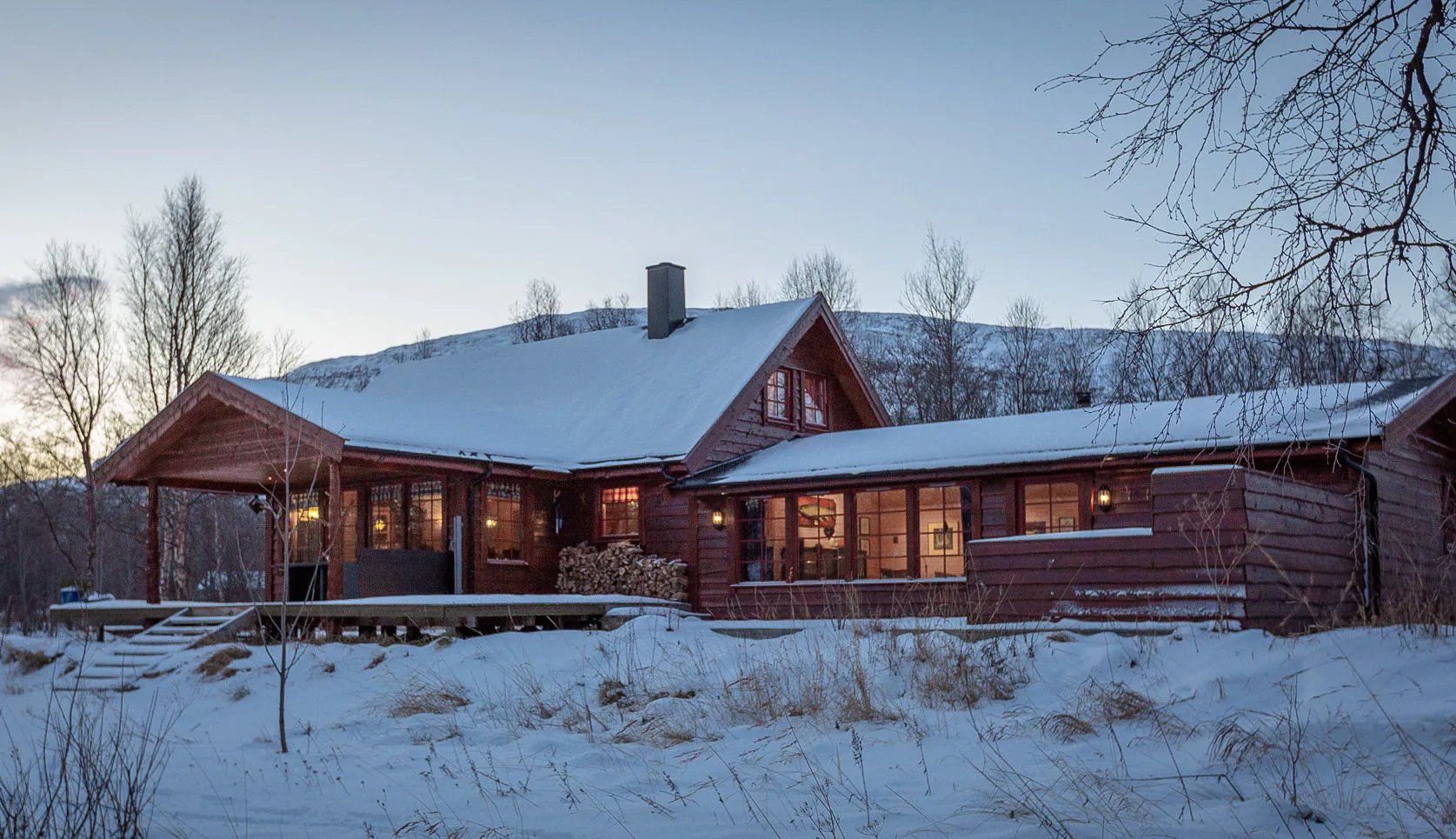Red wooden lodge building covered in snow at dusk with warm interior lights