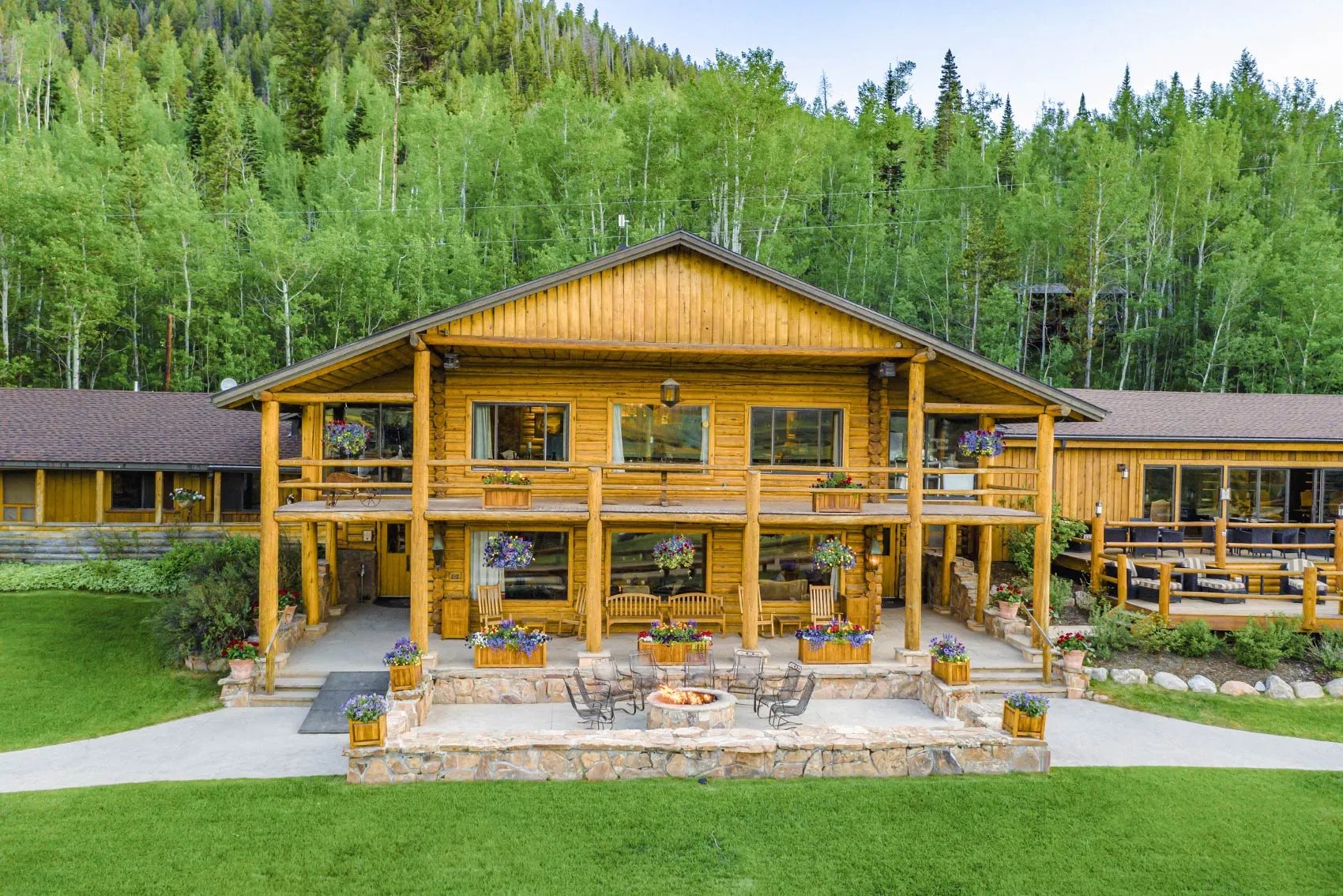 Grand wooden main lodge with multiple balconies and a stone patio, surrounded by forest.