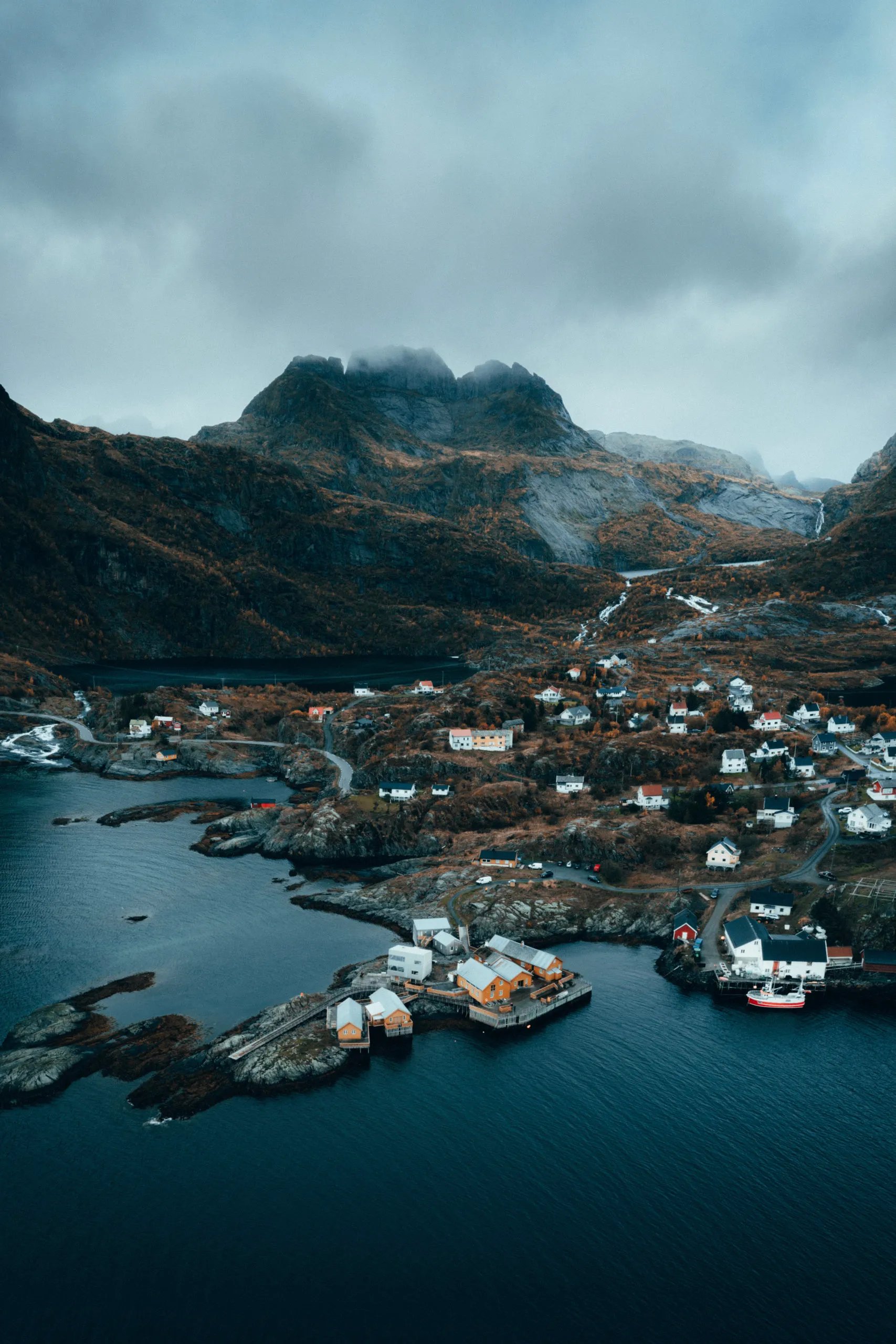 Aerial view of a picturesque fishing village nestled among dramatic mountains and a bay.