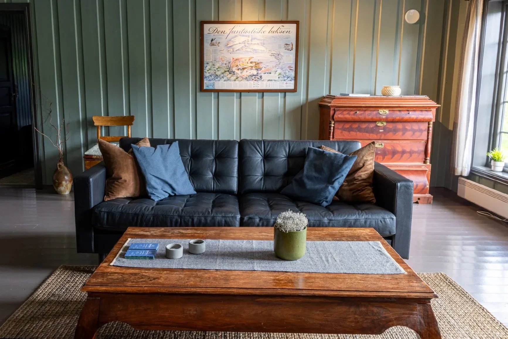 Cozy living room with a black leather sofa, wooden coffee table, and green paneled walls.