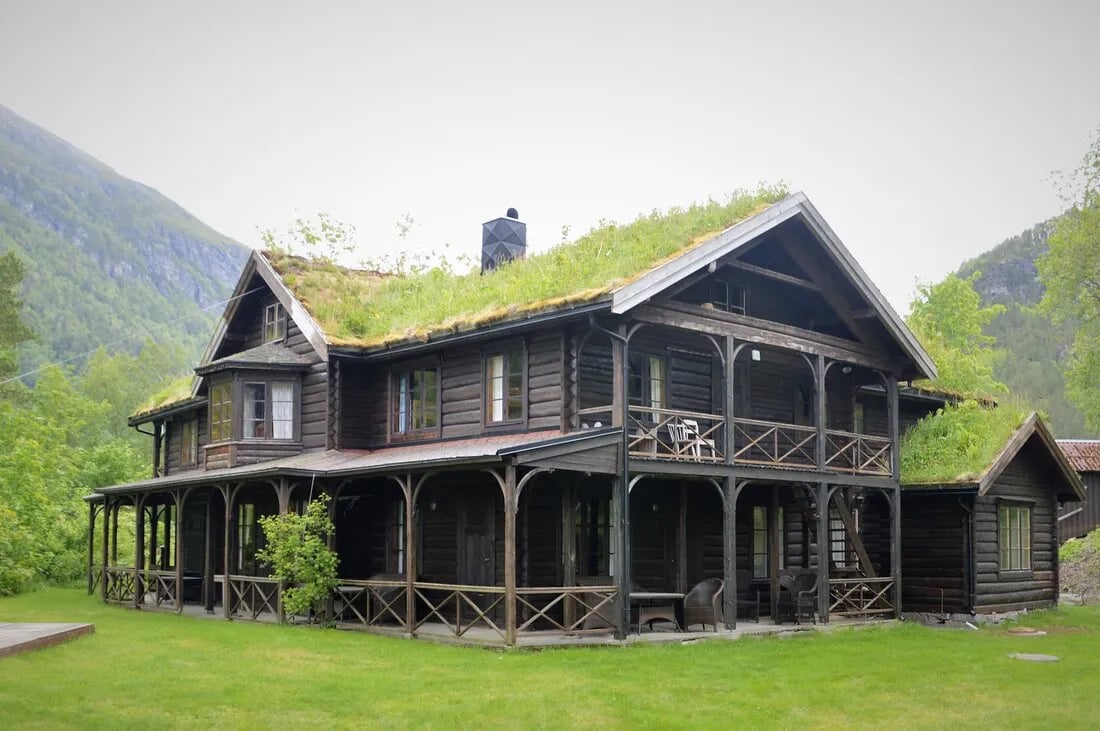 Dark wooden lodge with a vibrant green grass roof and multiple balconies, set against a green hillside.