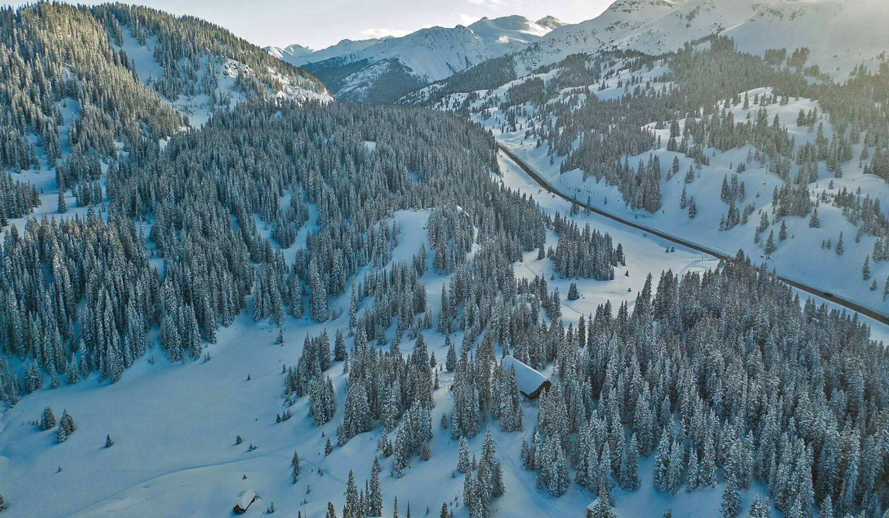Aerial view of a snowy mountain forest with a winding road and a small lodge