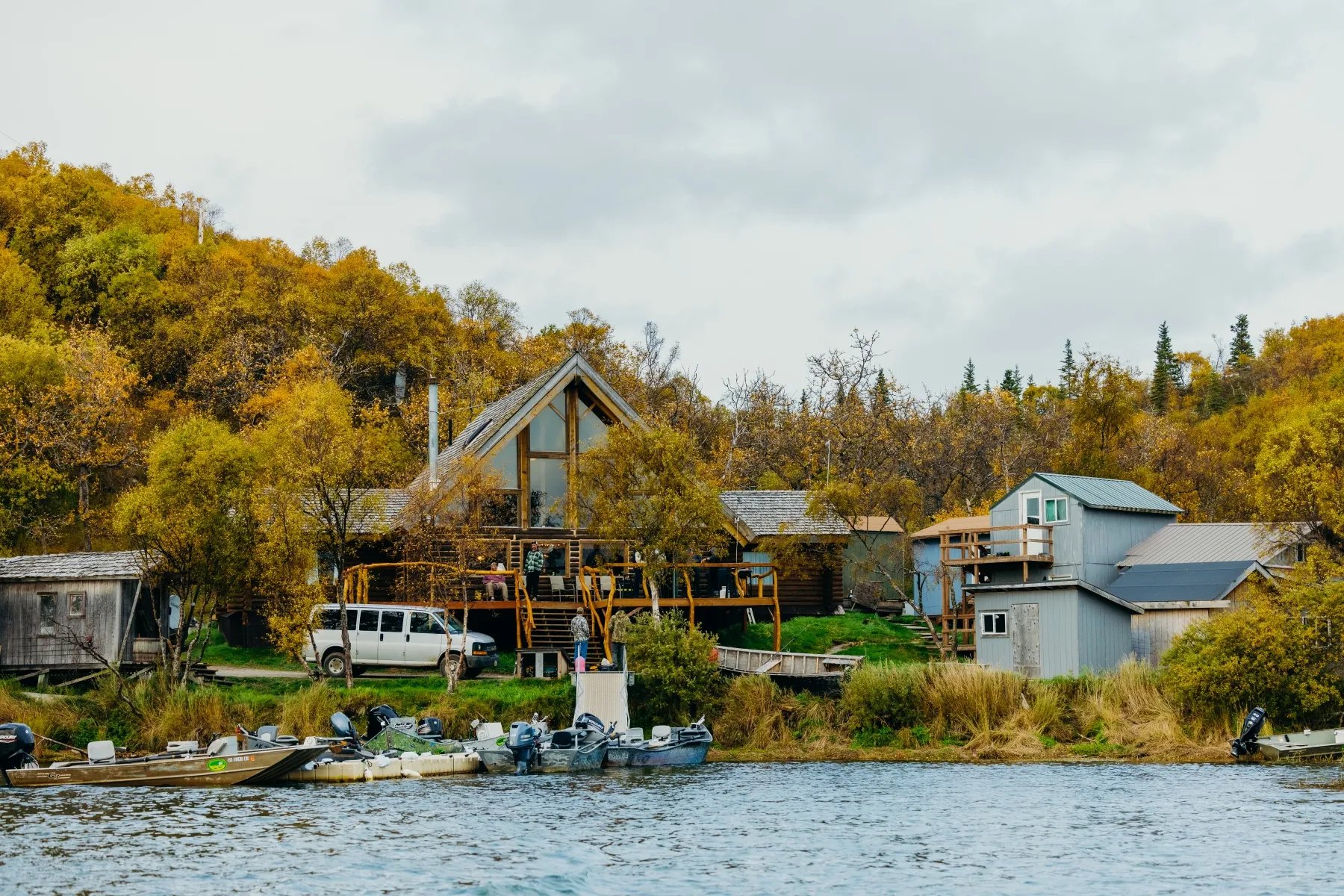 Katmai Trophy Lodge complex with multiple buildings and a white van, viewed from the river.
