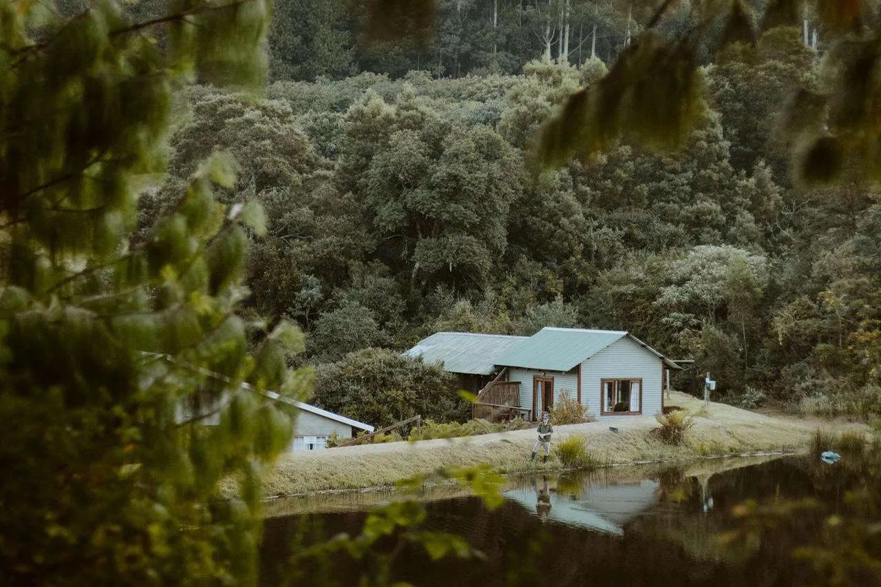 Wooden cabin on stilts with a wide deck, set on a sunny green hillside.