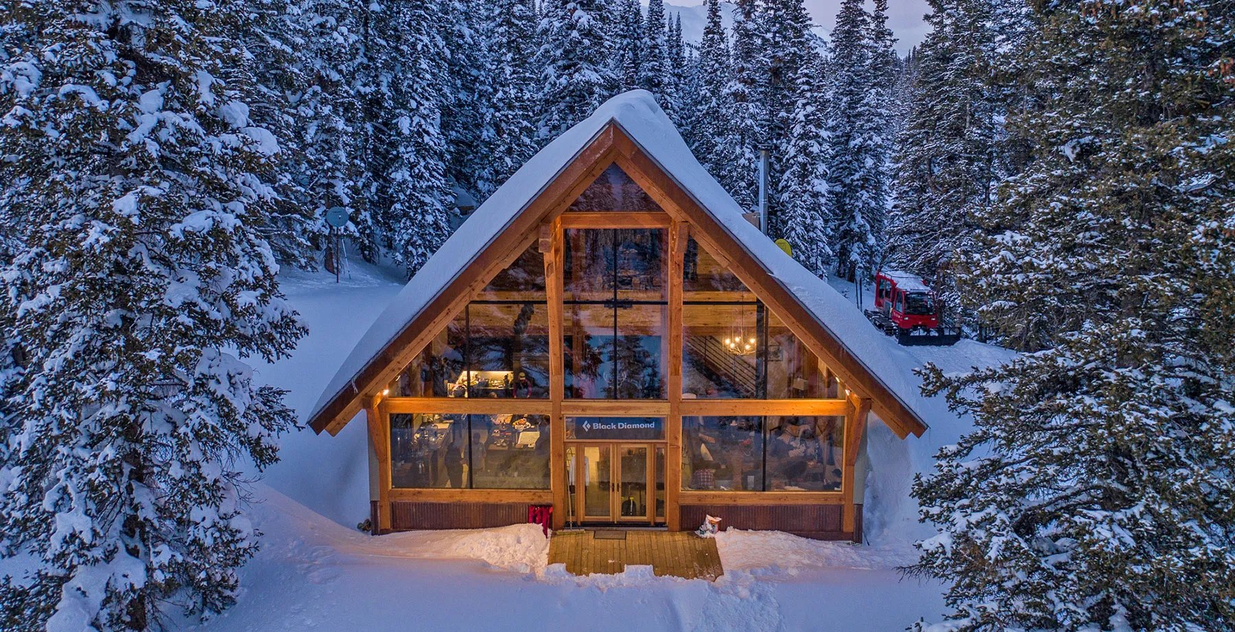 A-frame lodge exterior covered in snow, surrounded by tall pine trees on a clear day