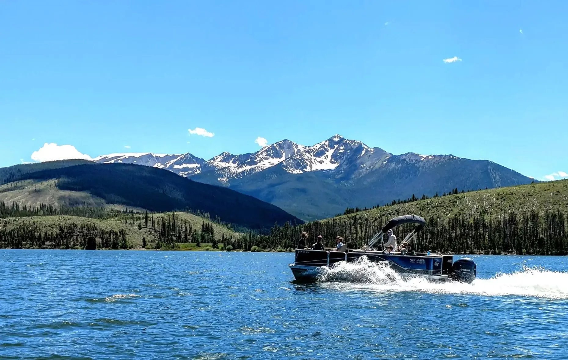 Pontoon boat on a large lake with snow-capped mountains under a blue sky